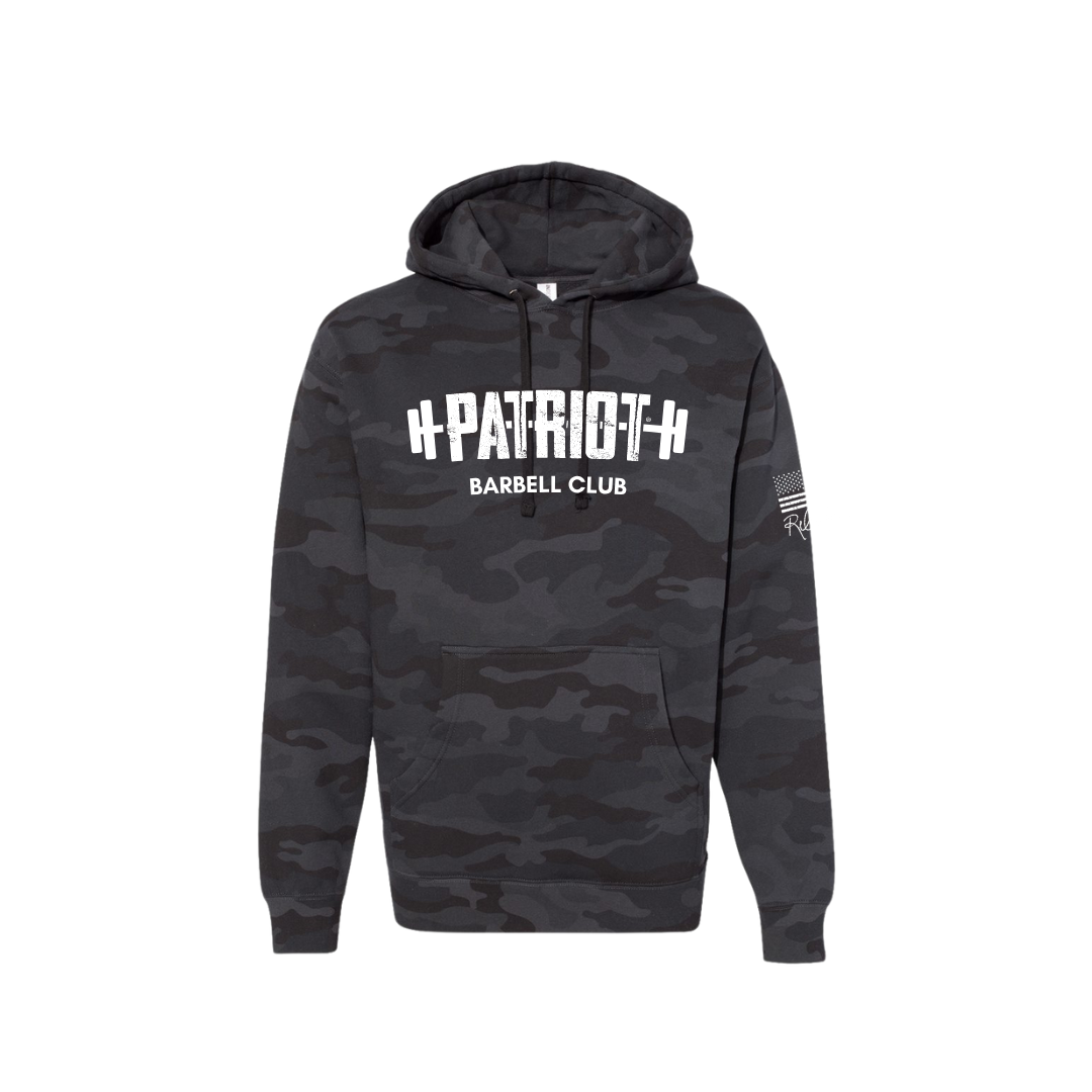 A camo hooded sweatshirt featuring the words Patriot barbell club across the chest. The word PATROT is part of a barbell design. The barbell goes right through the letters, so that the weights are on either side. The sleeve has a distressed flag and Rebecca's signature underneath.