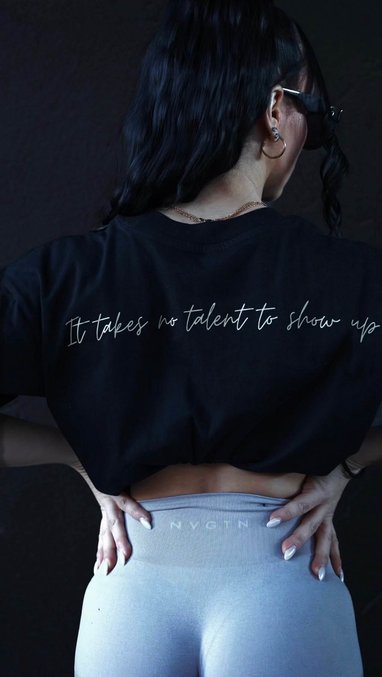 a photo featuring Mariana's back to show off her shirt. Black tee with "It takes no talent to show up" in a light gold script across the back.