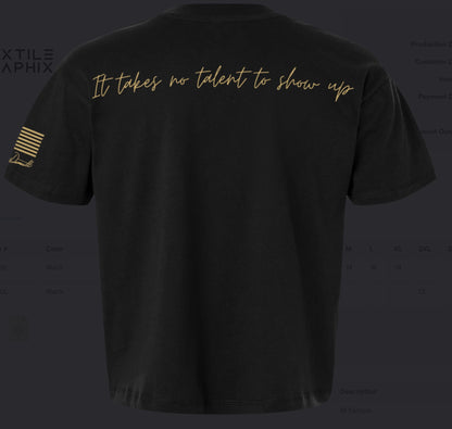 Black tee with "It takes no talent to show up" in a light gold script across the back and a matching PATRIOT distressed logo on the chest. The sleeve features a distressed American flag and Marianna's signature underneath. 